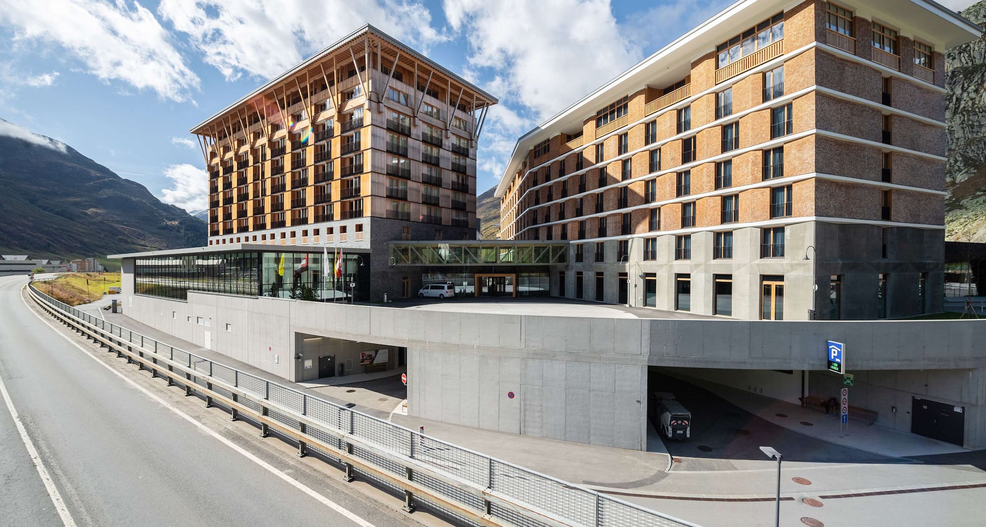 Aussenansicht des Radisson Blu Hotel Reussen in Andermatt mit seiner Holzfassade und den Bergen im Hintergrund.