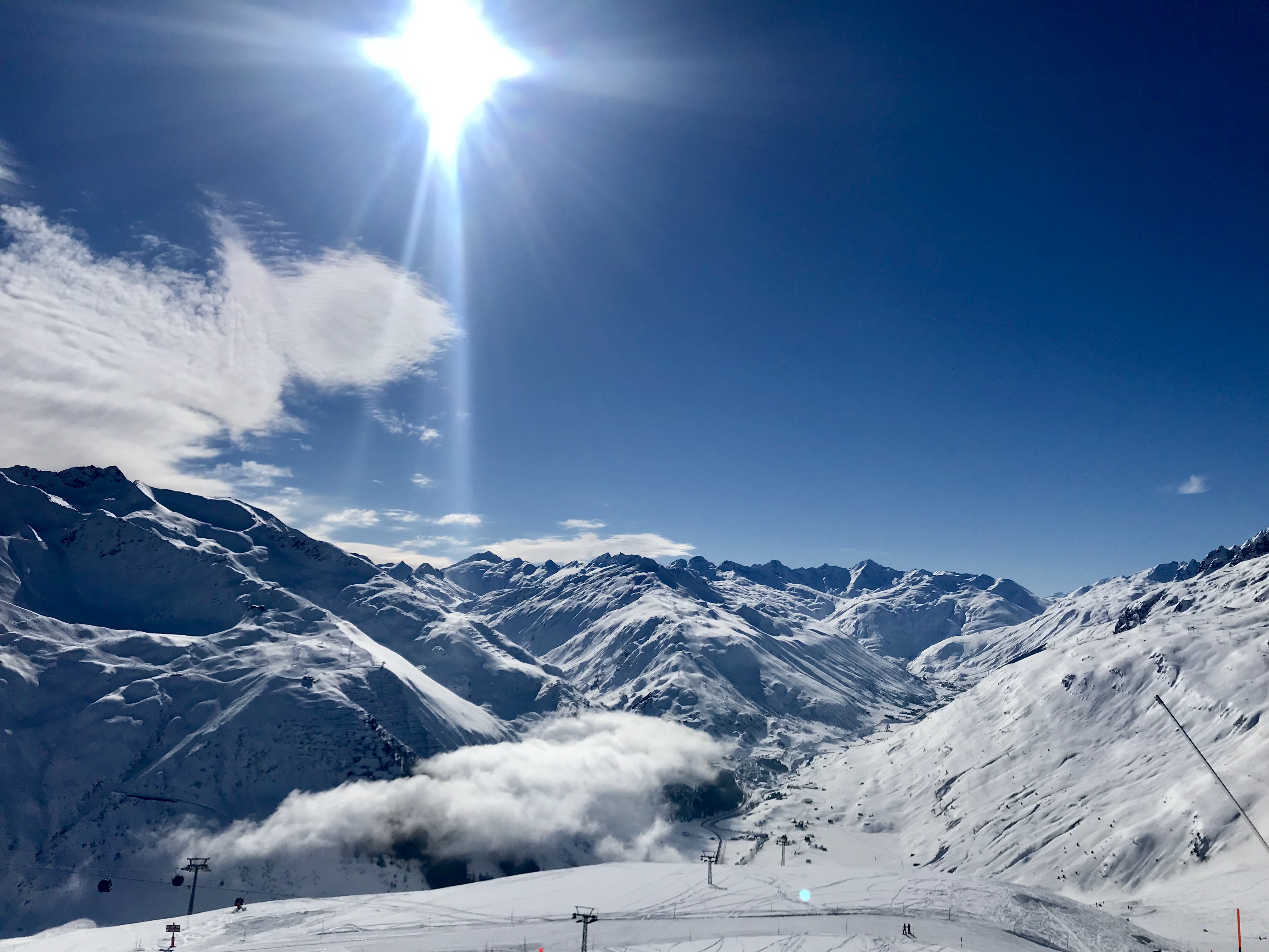 Sonniges Bergpanorama mit verschneiten Gipfeln und Skipisten unter blauem Himmel
